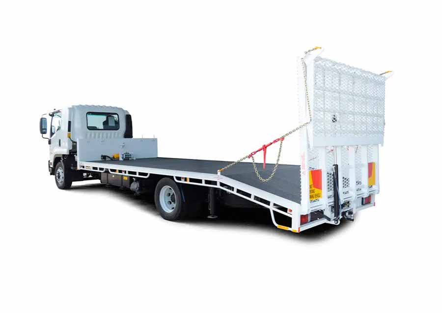 large beavertail trailer attached to a truck, the trailer does not have anything on it, it is shown from the rear angle